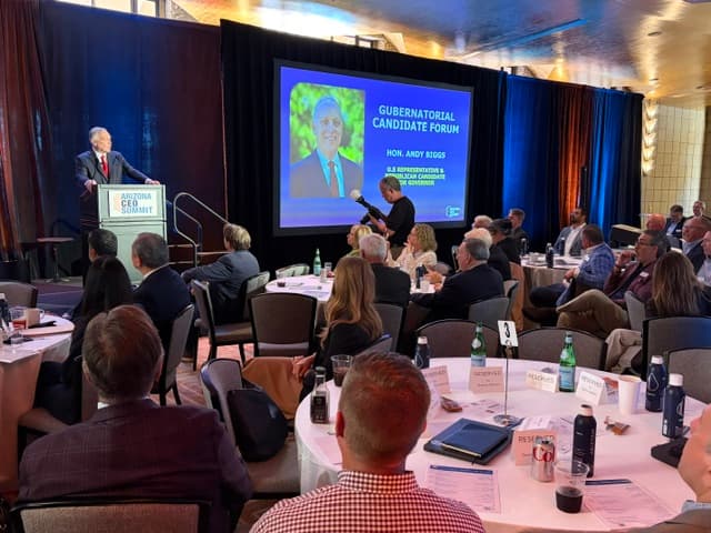 A speaker at the Arizona CEO Summit podium as the screen introduces Representative Andy Biggs for the Gubernatorial Candidate Forum.